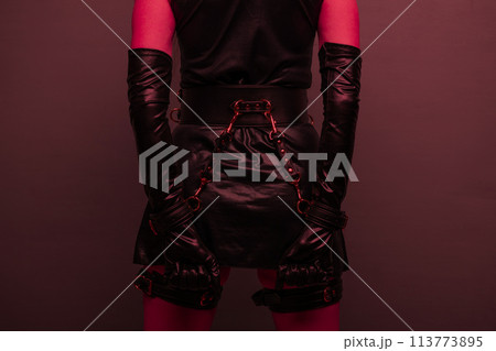 Beautiful young woman in a leather dress and bondage set posing back on red light backgound Beautiful young woman in a leather dress and bondage set posing back on red light backgound 113773895