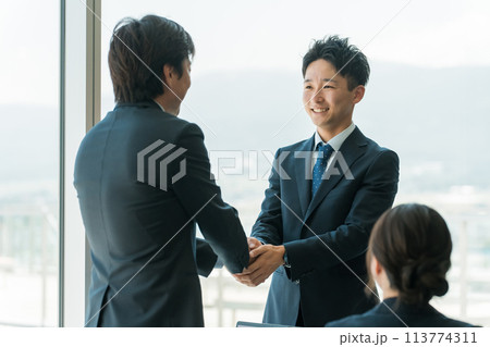 企業のオフィス・会議室で握手をして契約を結ぶビジネスマン 113774311