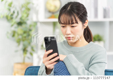深刻な表情でスマートフォンを見る女性 深刻な表情でスマートフォンを見る女性 113777147