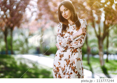 Beautiful young woman near the blooming spring tree. Attractive girl enjoying her time outside in park. 113777244