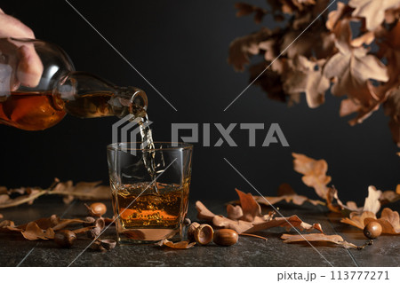 Whiskey on a black table with dried-up oak leaves. 113777271