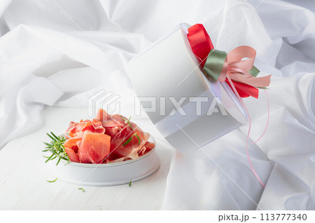 Prosciutto with rosemary in gift box on a white wooden table. 113777340