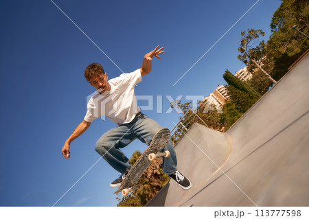 Excited young man riding skateboard in skate park on sunny day. Extreme sport concept Excited young man riding skateboard in skate park on sunny day. Extreme sport concept 113777598
