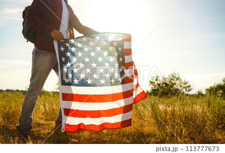 4th of July. American Flag. Traveler with the flag of America. The man in a hat, a backpack, a shirt and jeans. 113777673