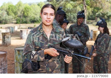 Woman paintball player standing with gun Woman paintball player standing with gun 113779060