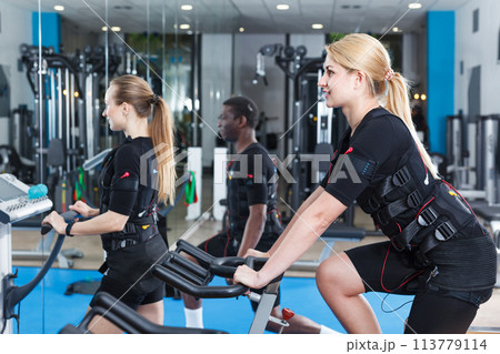 Two adult girls dressed EMS vests talking in gym Two adult girls dressed EMS vests talking in gym 113779114