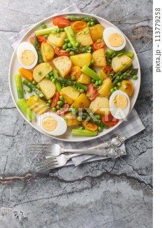 Fried potatoes with asparagus, cherry tomatoes, egg and green peas close-up in a plate. Vertical top view 113779258