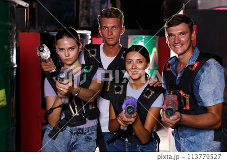 Young girls and guy standing with laser guns during laser tag game Young girls and guy standing with laser guns during laser tag game 113779527