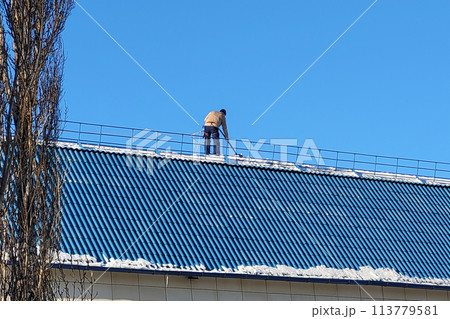 Orenburg, Russia - February 24, 2024 A worker removes snow from a city building with a shovel. Editorial Orenburg, Russia - February 24, 2024 A worker removes snow from a city building with a shovel. Editorial 113779581