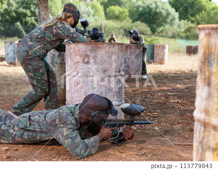 Two opposing teams shooting on paintball playing field outdoors Two opposing teams shooting on paintball playing field outdoors 113779843