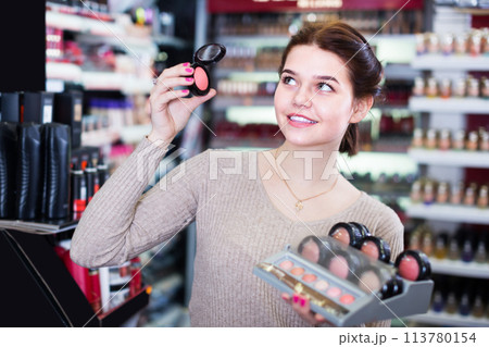 cheerful female customer deciding on make-up items in cosmetics shop 113780154