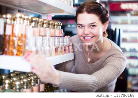 cheerful woman customer deciding on perfume variants in cosmetics shop cheerful woman customer deciding on perfume variants in cosmetics shop 113780169