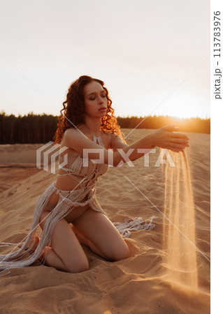 Sexy woman is kneeling in the sand, holding sand in her hands 113783976