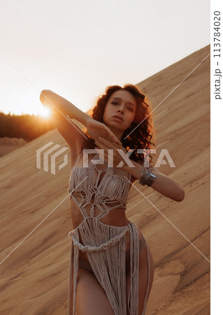 Sexy woman in a rope dress poses on a sandy hillside. 113784020