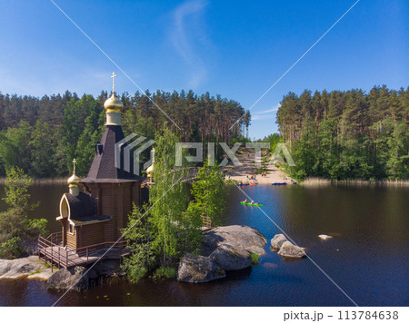 Aerial top view to wooden Church of St. Apostle Andrew First-Called on Vuoksa River with bridge. Temple on small island near village Vasilevo, Melnikovo, Priozersky District Leningrad region. Russia Aerial top view to wooden Church of St. Apostle Andrew First-Called on Vuoksa River with bridge. Temple on small island near village Vasilevo, Melnikovo, Priozersky District Leningrad region. Russia 113784638