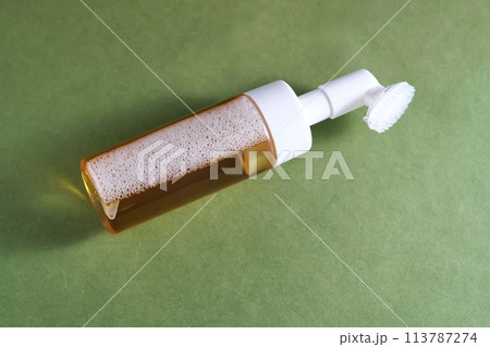Beige facial foam with a dispenser and brush in a green background. Beige facial foam with a dispenser and brush in a green background. 113787274