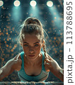 Focused female gymnast on balance beam, spotlighted by gym lights, demonstrates intense concentration 113788695