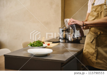 Close-up male chef wiping wet hands with kitchen towel while cooking dinner at home kitchen. People and domestic life. Culinary concept 113790553