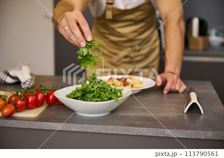 Close-up chef hands holding fresh arugula leaves, garnishing meal, cooking Italian spaghetti in the home kitchen. 113790561