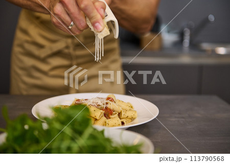 Close-up chef's hands seasoning and decorating meal with parmesan cheese and fresh arugula leaves, cooking pasta with tomato sauce according to traditional Italian recipe. Cuisine. Culinary. Epicure Close-up chef's hands seasoning and decorating meal with parmesan cheese and fresh arugula leaves, cooking pasta with tomato sauce according to traditional Italian recipe. Cuisine. Culinary. Epicure 113790568