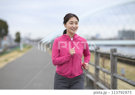 スポーツウエアで土手をランニングをするミドル女性 113792973