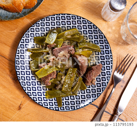 There is plate with braised french green bean and beef tenderloin stew on wooden table. 113795193