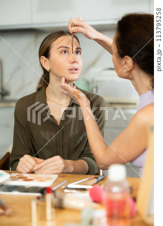 Adult woman doing makeup to young woman Adult woman doing makeup to young woman 113795258