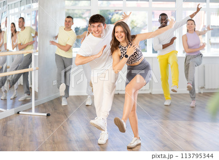 Happy enthusiastic young girl and guy honing hip-hop moves in dance studio setting with group of women and men 113795344