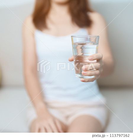 Happy woman holding water glass, female drinking pure water on sofa at home. Healthy, Refreshment, lifestyle and daily routine concept Happy woman holding water glass, female drinking pure water on sofa at home. Healthy, Refreshment, lifestyle and daily routine concept 113797162