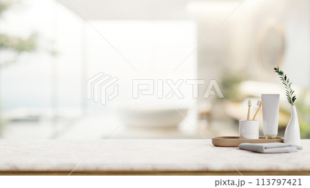 A toothpaste, toothbrushes, a towel on a white tabletop in a contemporary bathroom with a bathtub. A toothpaste, toothbrushes, a towel on a white tabletop in a contemporary bathroom with a bathtub. 113797421