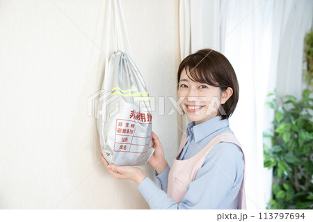 壁に掛けた非常持ち出し袋を持つ女性 113797694