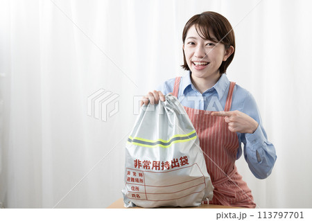 壁に掛けた非常持ち出し袋を持つ女性 壁に掛けた非常持ち出し袋を持つ女性 113797701