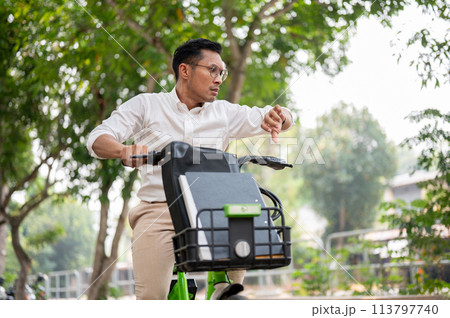 A stressed businessman is in a hurry to get to work, riding a bike, checking time on his wristwatch. A stressed businessman is in a hurry to get to work, riding a bike, checking time on his wristwatch. 113797740
