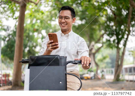 A happy, carefree Asian businessman is checking messages on his smartphone while he is on a bike. 113797742