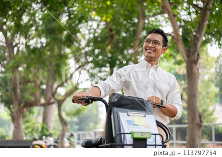 A happy, carefree Asian businessman pushing his bike, walking in the public park. A happy, carefree Asian businessman pushing his bike, walking in the public park. 113797754