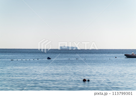 Calm blue sea with the silhouette of a large ship on the horizon Calm blue sea with the silhouette of a large ship on the horizon 113799301