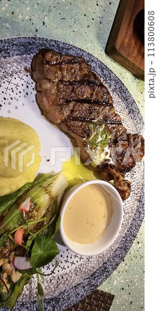 Beef New York strip loin steak or sirloin steak served with potatoes, and mushroom sauce and salad on plate Beef New York strip loin steak or sirloin steak served with potatoes, and mushroom sauce and salad on plate 113800608
