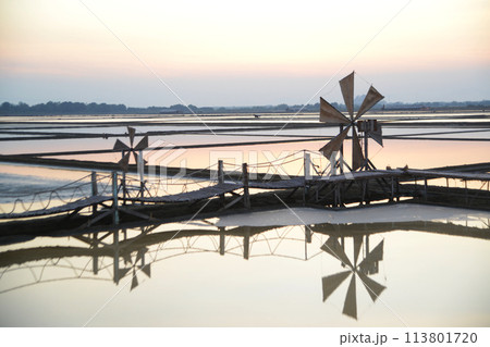 Sunset over the wooden turbines used to push seawater up into the salt fields during the hot summer months of Thailand, a beautiful landscape of the salt fields. Traditional salt farming culture. 113801720