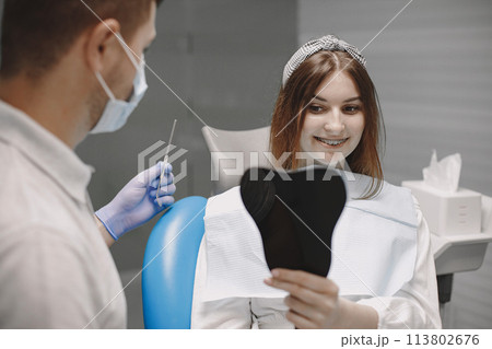 Female patient looking in a mirror while sitting in the dental chair 113802676