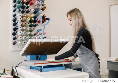 Young dressmaker standing in workshop near the bright wall with threads Young dressmaker standing in workshop near the bright wall with threads 113802715