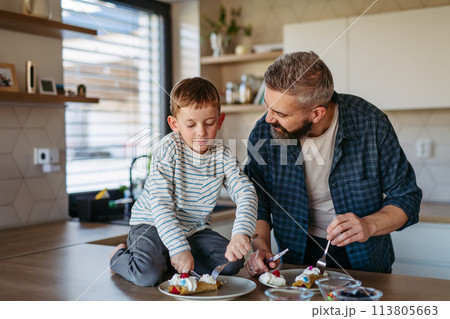 Boy filling pancake with fruit, sweets. Father spending time with son at home, making snack together, cooking. Fathers day concept. 113805663