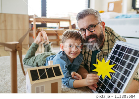 Father explaining renewable energy, solar power and teaching about sustainable lifestyle his young son. Playing with model of house with solar panels. Father explaining renewable energy, solar power and teaching about sustainable lifestyle his young son. Playing with model of house with solar panels. 113805684