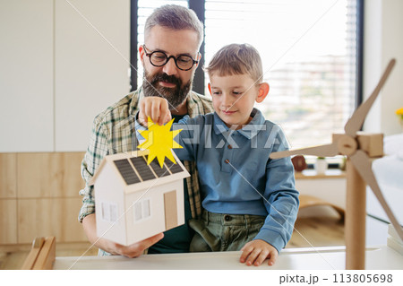 Father explaining renewable energy, teaching about sustainable lifestyle his young son. Playing with house with solar panels, wind turibine at home. 113805698