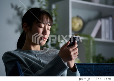スマートフォンを見ながら目を閉じる女性 113807376