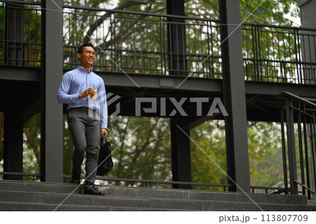 Confident smiling young businessman walking down the staircase outside his office Confident smiling young businessman walking down the staircase outside his office 113807709