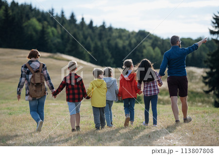 Young students walking across meadow during biology field teaching class, holding hands. Dedicated teachers during outdoor active education teaching about ecosystem, ecology. 113807808