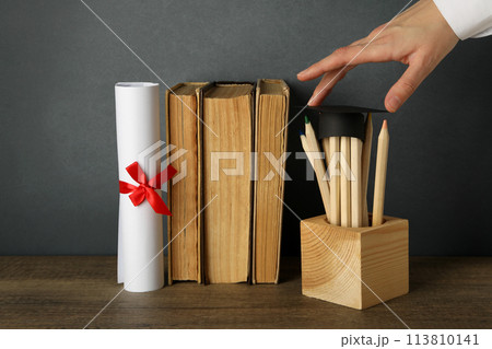Graduation hat with books on a table on a dark background. Graduation hat with books on a table on a dark background. 113810141