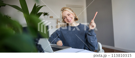 Portrait of young smiling woman, student talking to teacher online via video chat, doing course, attends remote course in internet, making notes Portrait of young smiling woman, student talking to teacher online via video chat, doing course, attends remote course in internet, making notes 113810315