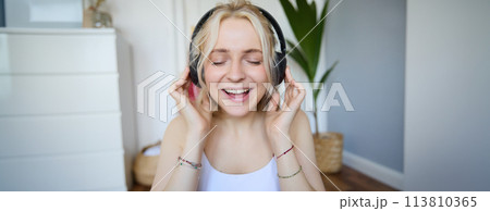 Close up portrait of woman smiling while listening to music in wireless headphones, singing with eyes closed 113810365