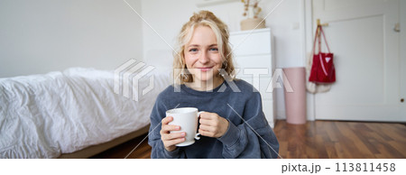 Image of young teenage girl sitting in her bedroom on floor, drinking cup of tea and enjoying day at home, smiling and looking at camera Image of young teenage girl sitting in her bedroom on floor, drinking cup of tea and enjoying day at home, smiling and looking at camera 113811458